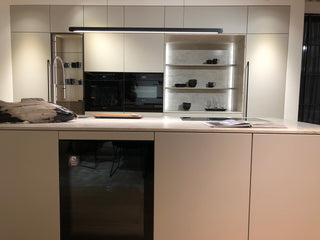 Unsere Loftküche im Obergeschoss mit großer Kücheninsel mit Taj Mahal Stein und großer Küchenfront mit Hochschränken, Vitrinenschrank und beleuchteter Küchennische aus Stein.